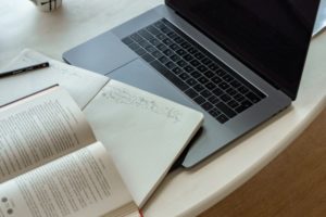 A laptop with a paper and book on top
